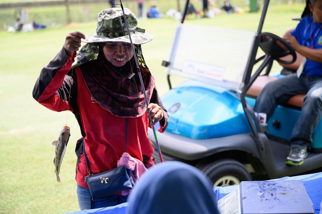 A lady picking up a caught fish with a golf buggy