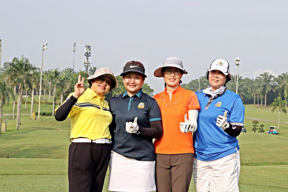 Four women are Posing on a Golf course with lush greenery.